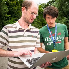 Teacher and engineer collaborating with racing car data on a laptop